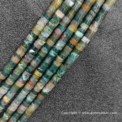 Angled view of natural ocean jasper flat disc gemstone strands arranged parallel on dark background