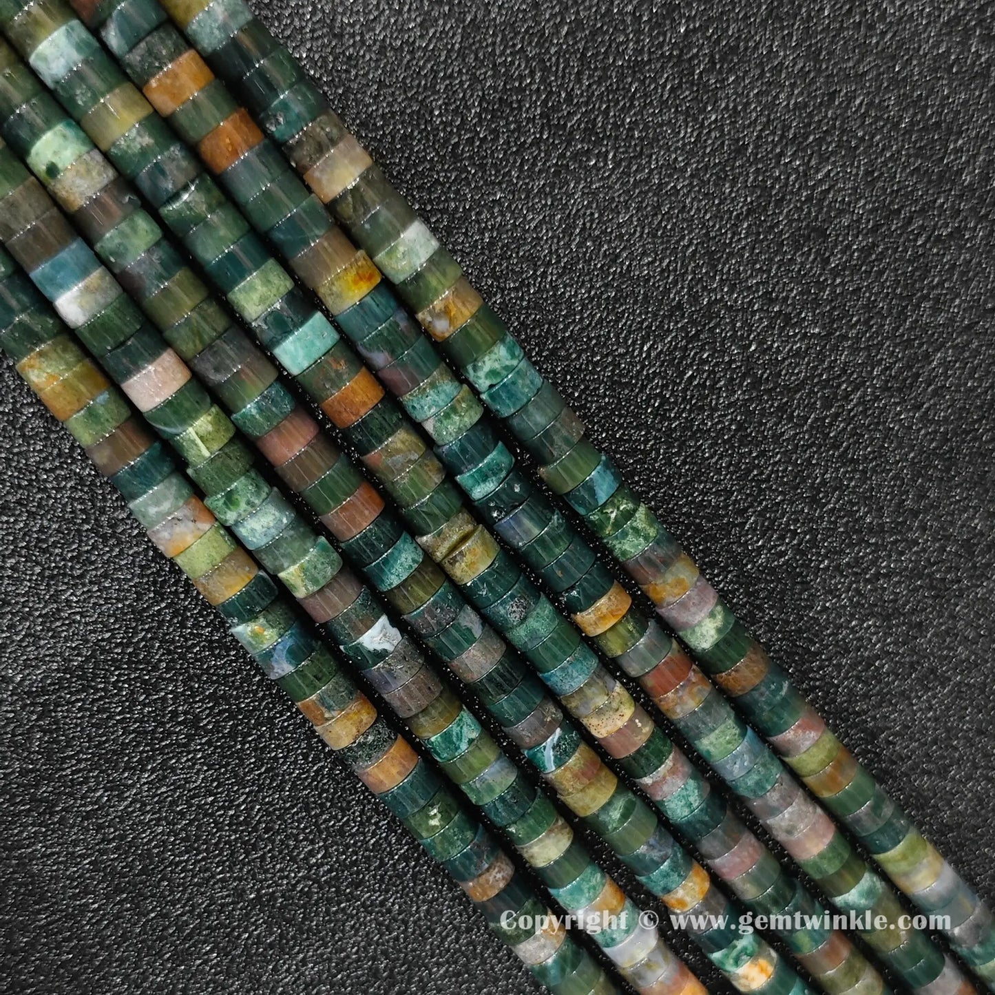Perspective view of ocean jasper heishi spacer beads showing uniform disc thickness and green hues