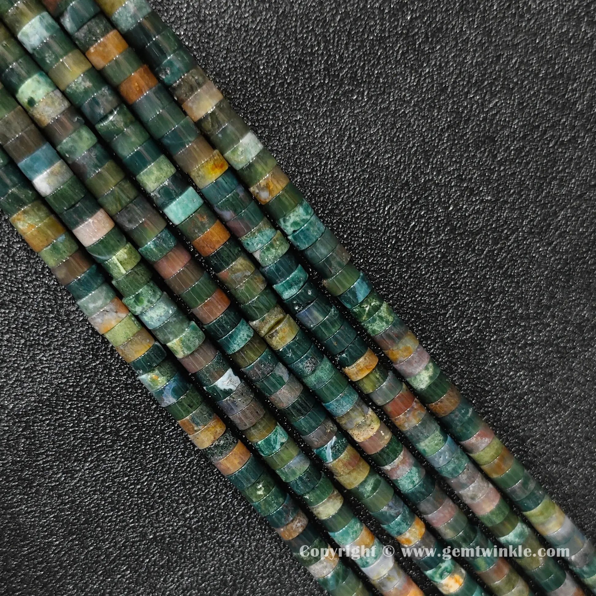Perspective view of ocean jasper heishi spacer beads showing uniform disc thickness and green hues