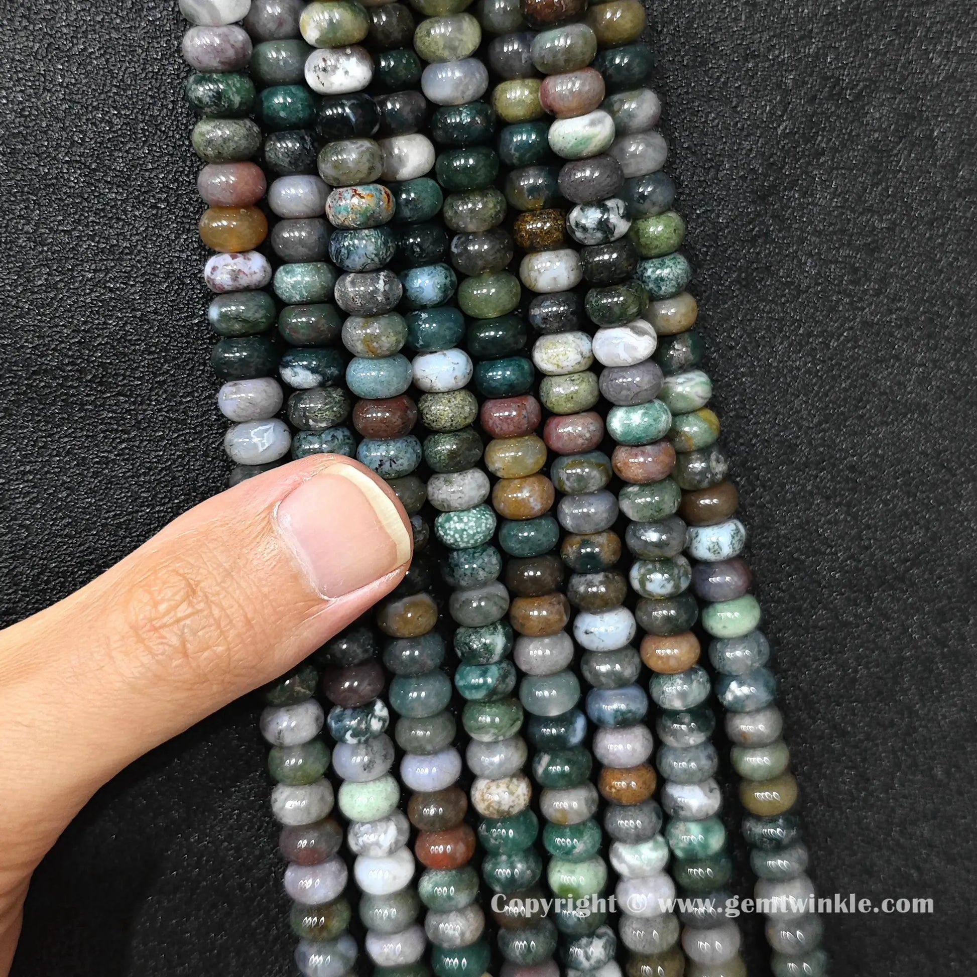 Close up view of 8x6mm ocean jasper smooth disc rondelle beads inspected on fingers for quality preview