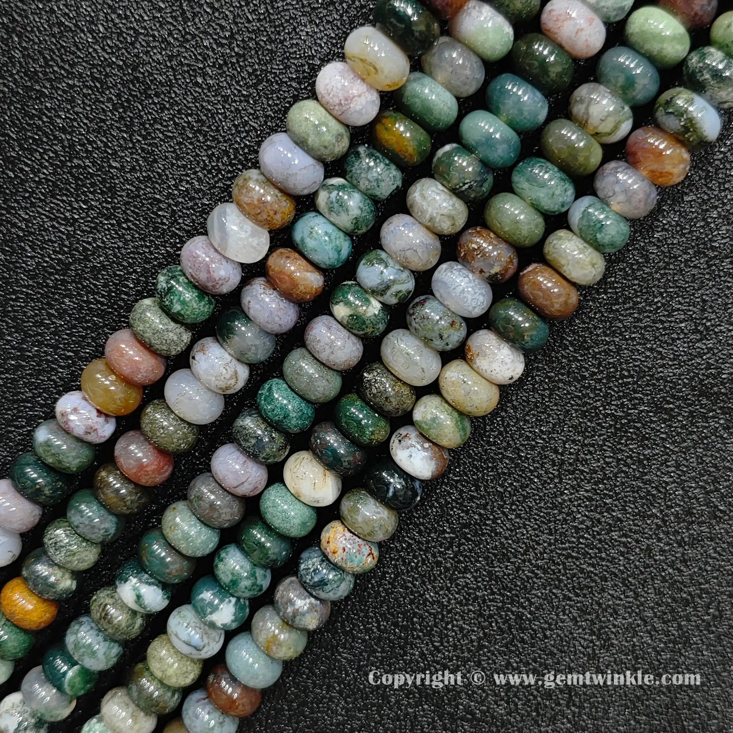 Angled view of natural ocean jasper smooth disc gemstone strands arranged parallel on dark background