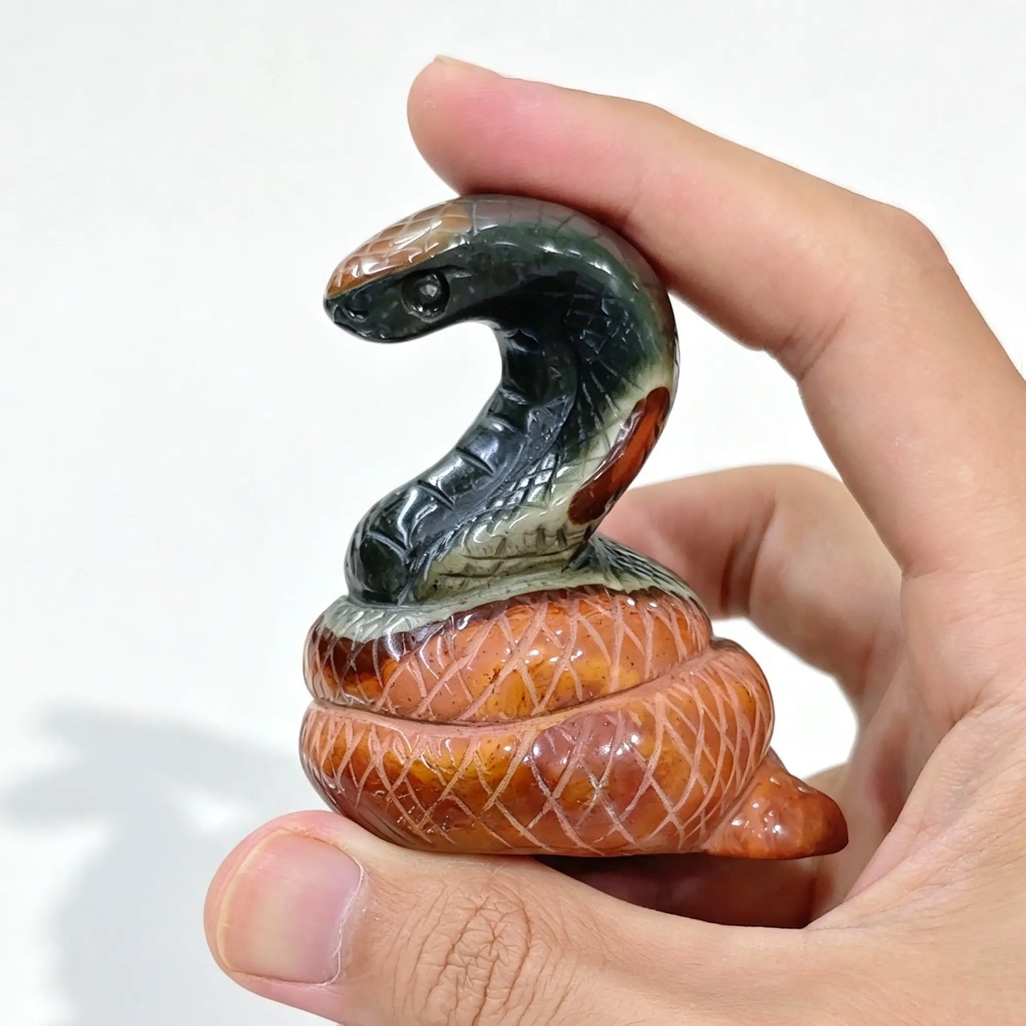 Ocean jasper snake statue held in hand showing dark green upright head and red patterned coiled base