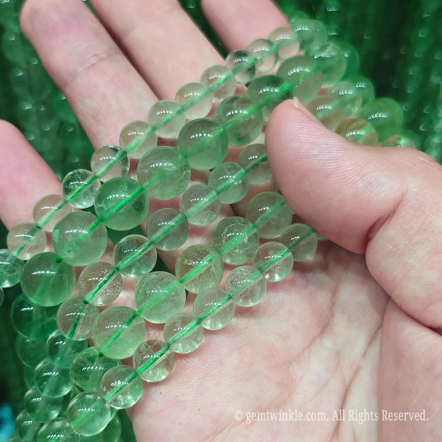 Hand holding translucent green fluorite loose beads strands showing natural light green colors and minimal cotton inclusions under natural light
