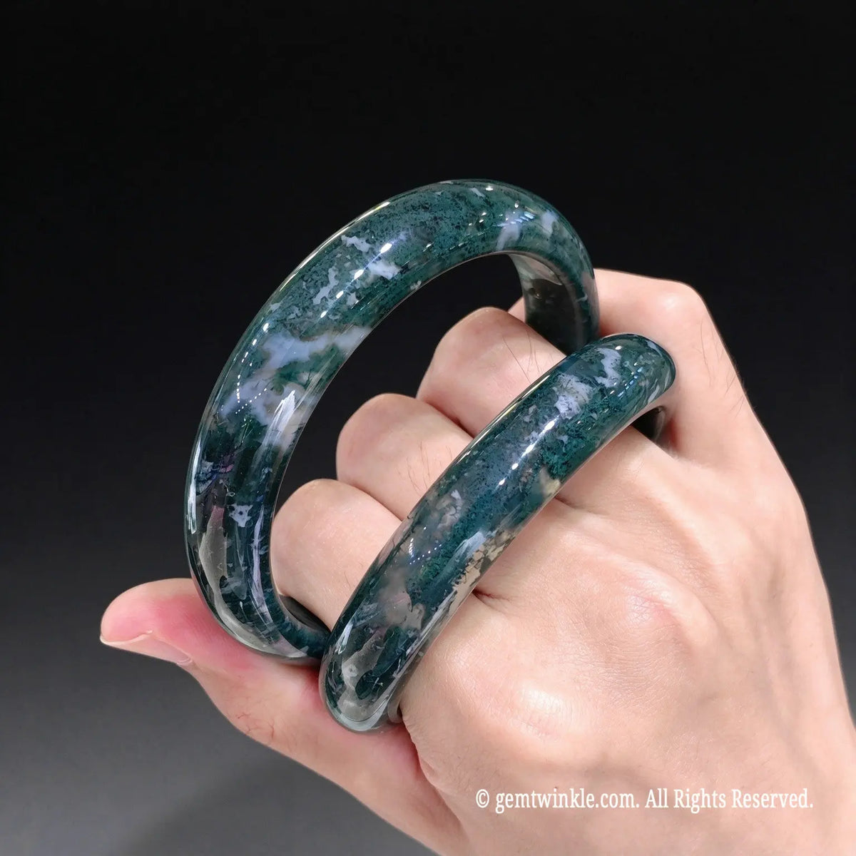 Perspective view of one piece green chalcedony gemstone bangles held across fingers displaying organic moss inclusions