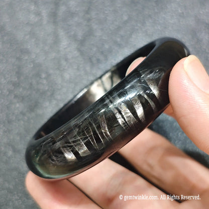 Perspective shot of one piece hypersthene gemstone bangle resting across fingers under studio lighting