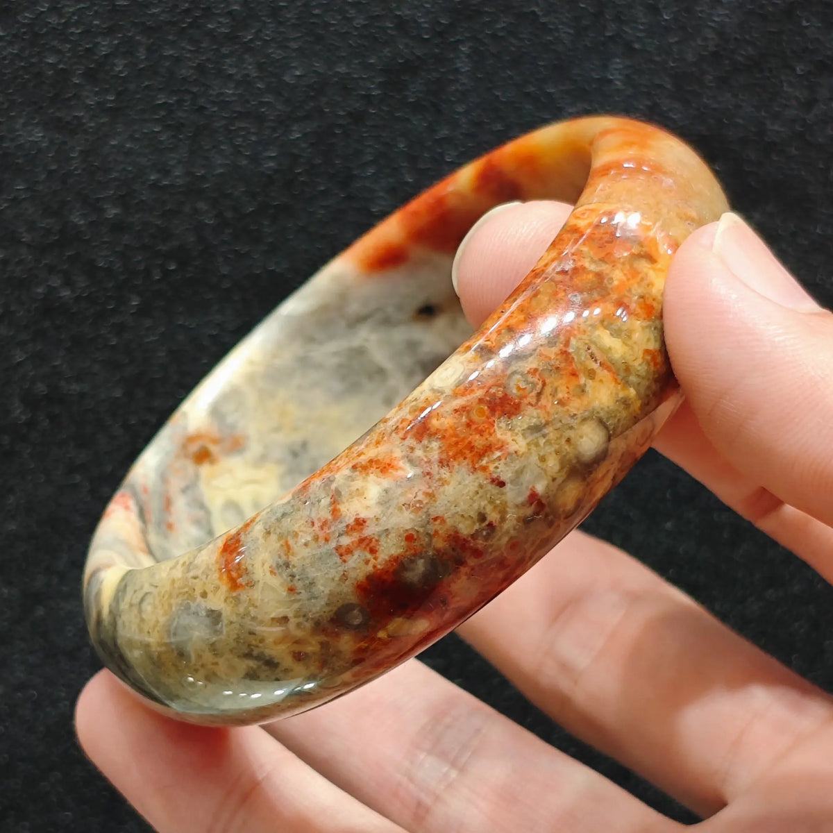hand holding exact piece red speckled crazy lace agate bangle showing lava mottled pattern