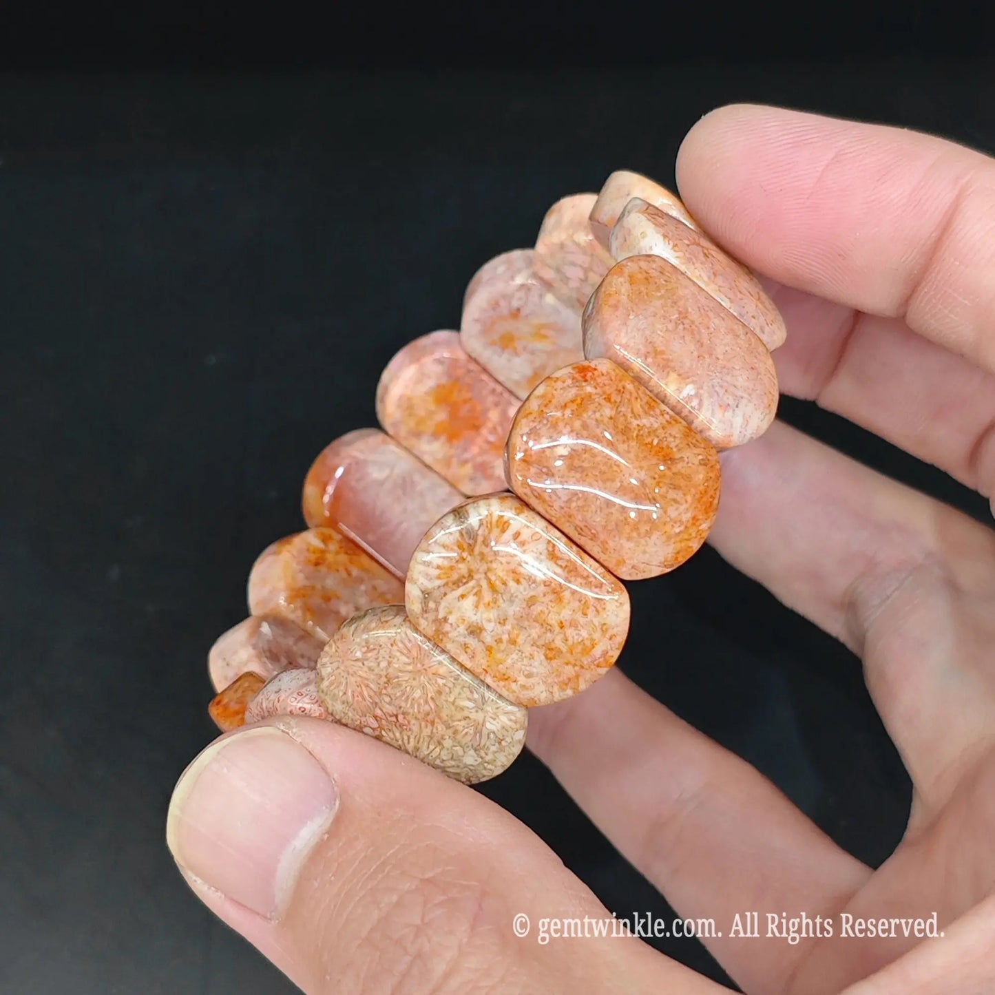 Orange fossil coral block cuff bracelet held in hand under studio light showing glossy surface polish and starburst inclusions