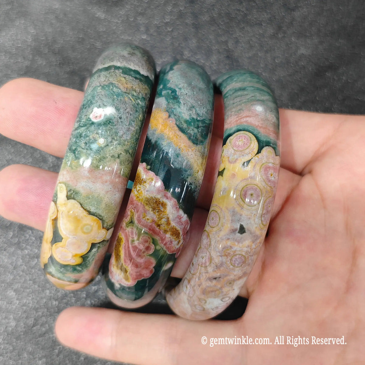 Side view of solid carved orbicular ocean jasper bangles held over fingers displaying colorful mineral swirls