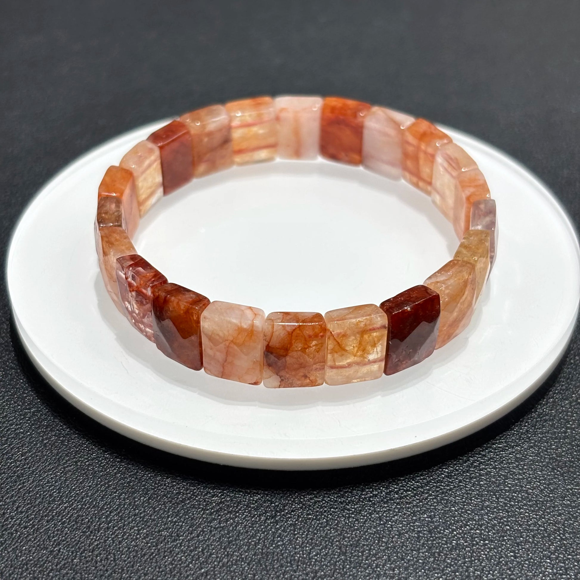 A red hematoid fire quartz bracelet with oval beads displayed on a white plate, highlighting the natural stone colors.