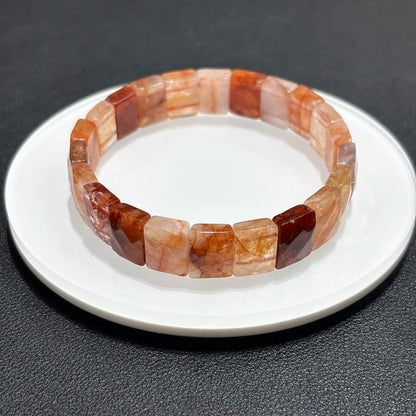 A red hematoid fire quartz bracelet with oval beads displayed on a white plate, highlighting the natural stone colors.