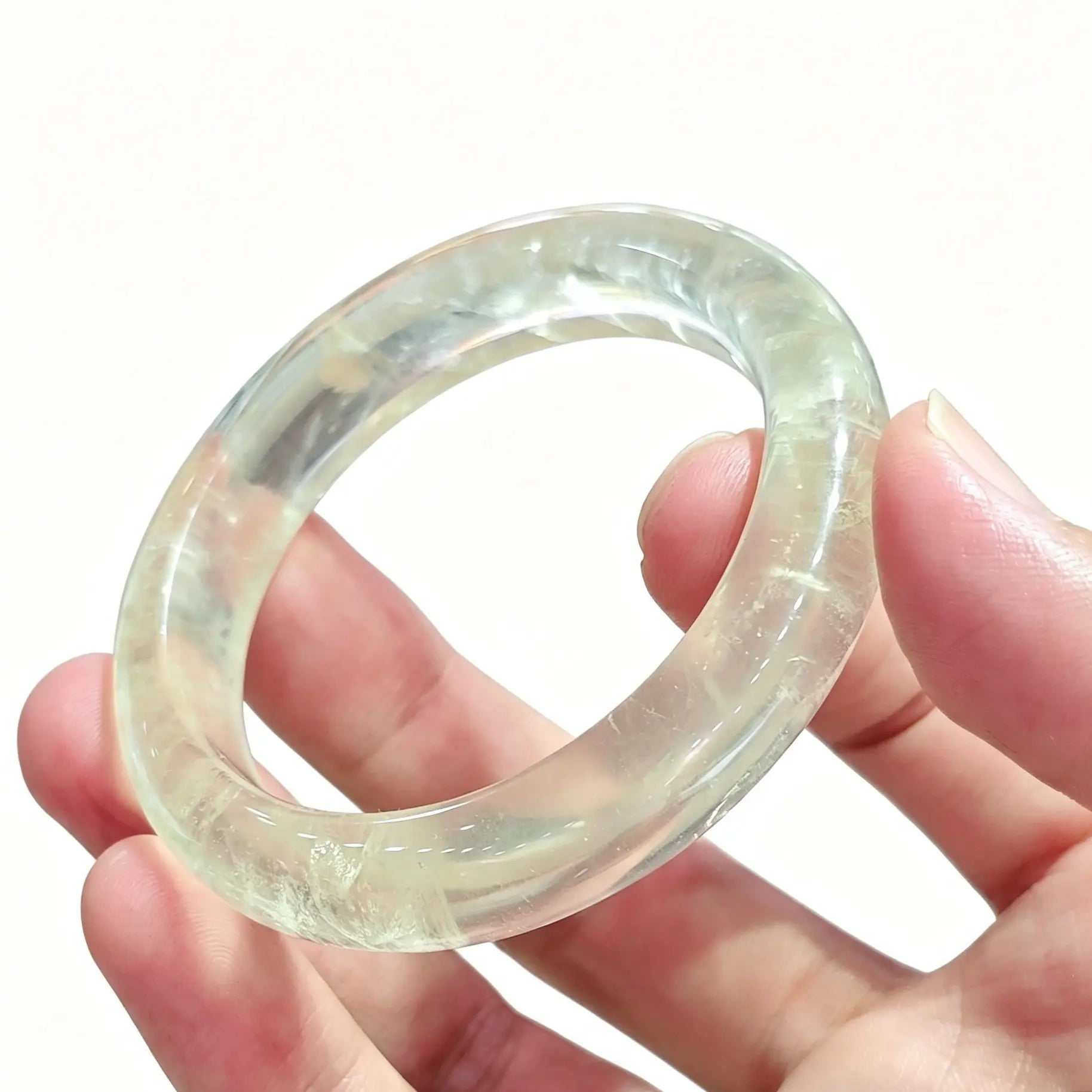 Fingers holding a translucent lemon quartz solid crystal bangle displaying bright yellow color with high transparency