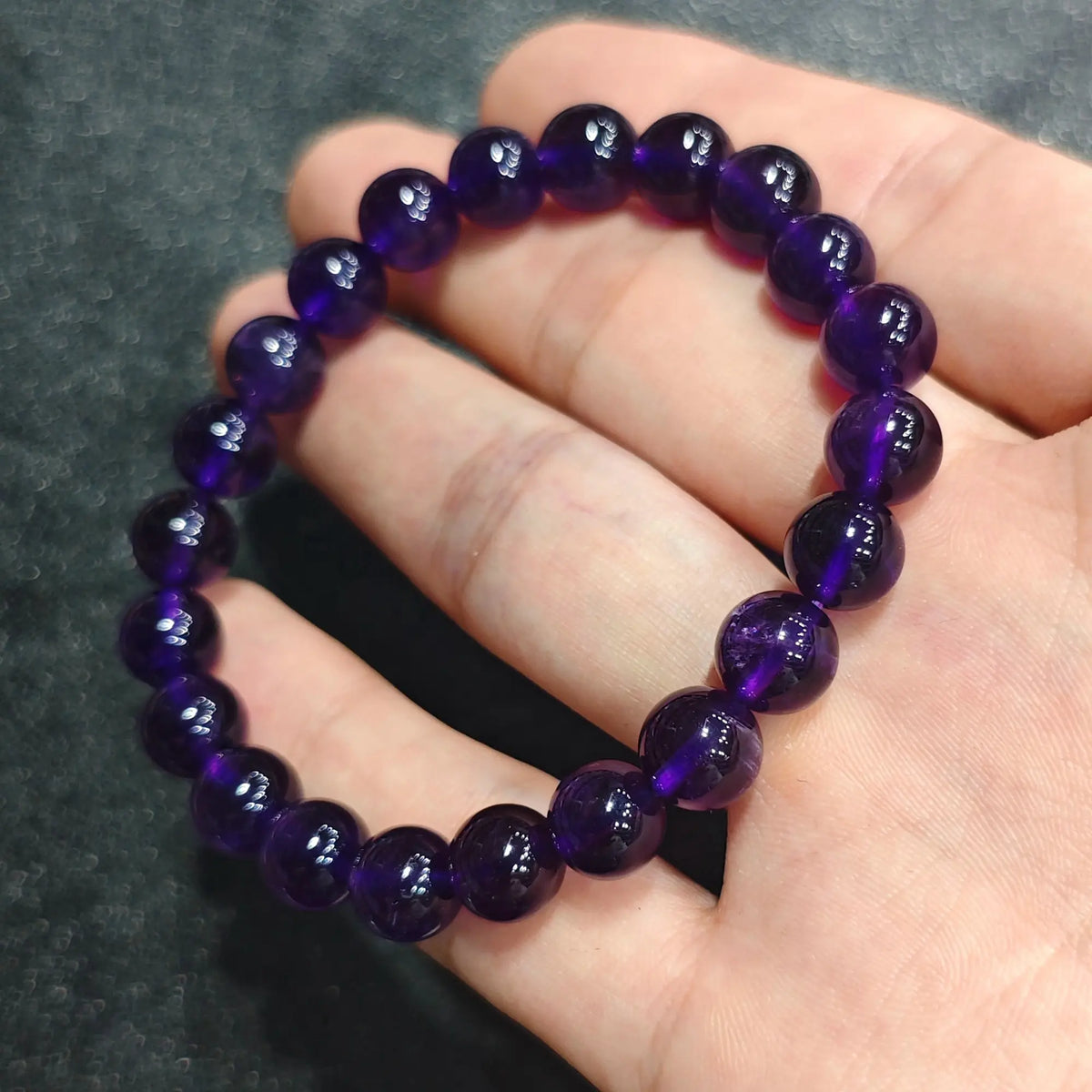 Close up view of a hand holding a high clarity natural deep purple amethyst bracelet with 8mm polished beads[cite: 8]