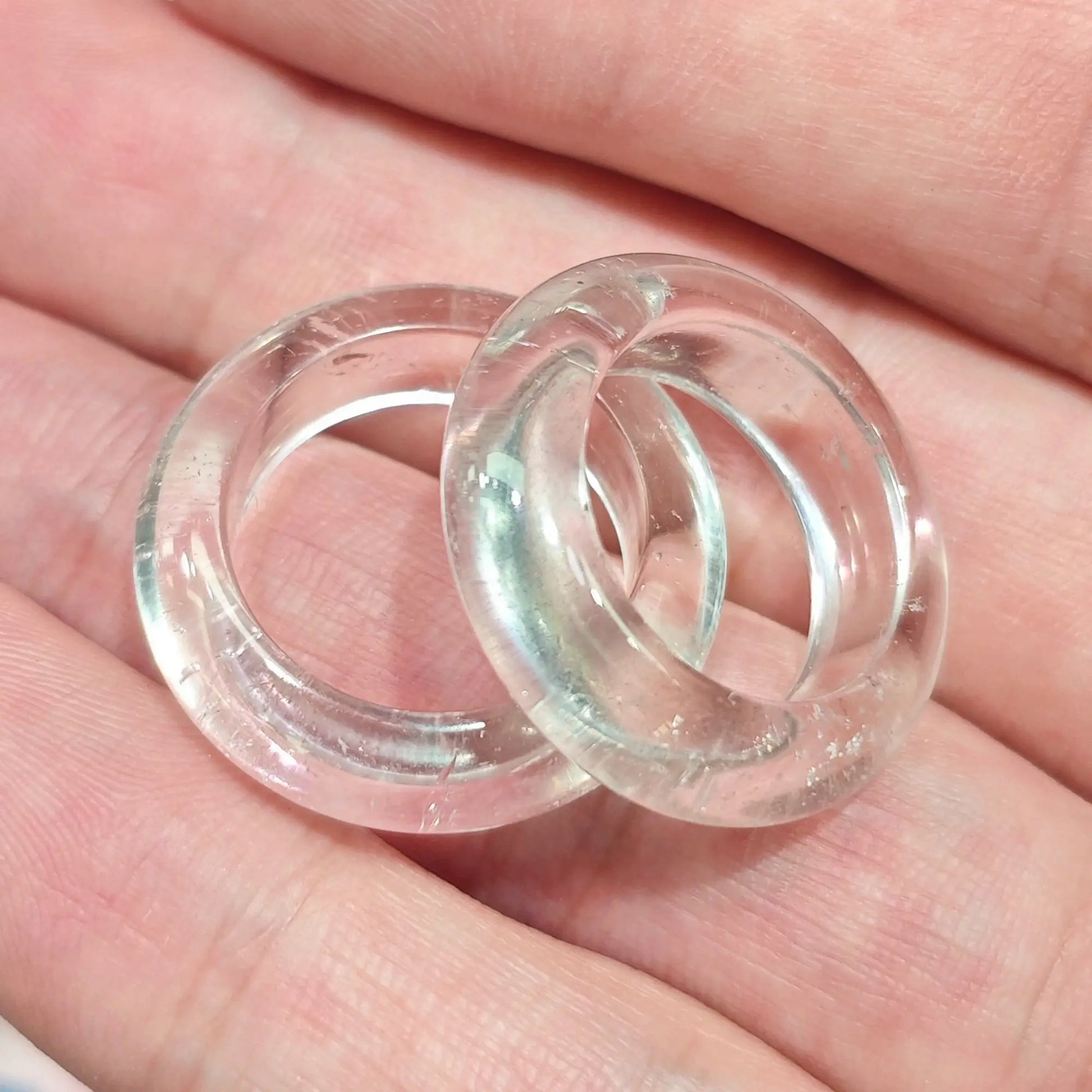 Hand holding two clear quartz solid gemstone rings showing polished transparency and natural subtle clouding