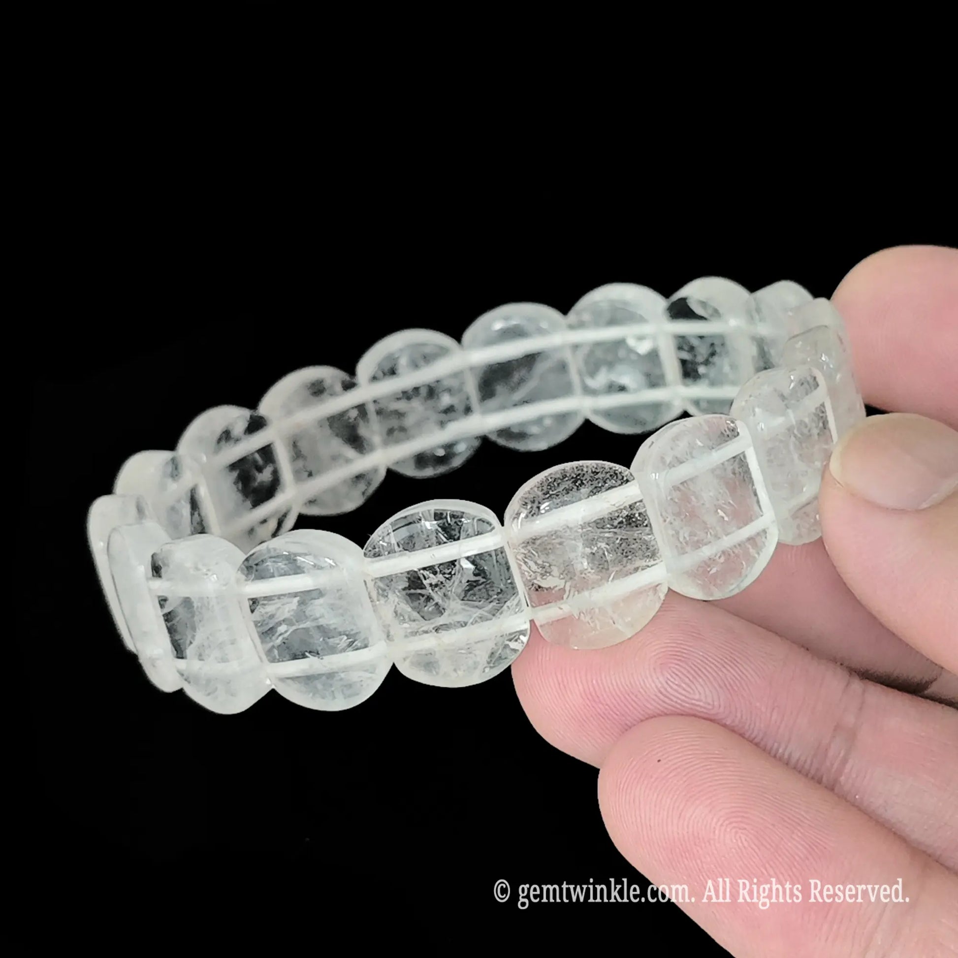 Natural clear quartz 14mm smooth rectangular bead bracelet held close up showing internal ice fractures and glossy polished finish