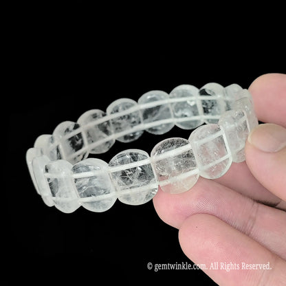Natural clear quartz 14mm smooth rectangular bead bracelet held close up showing internal ice fractures and glossy polished finish
