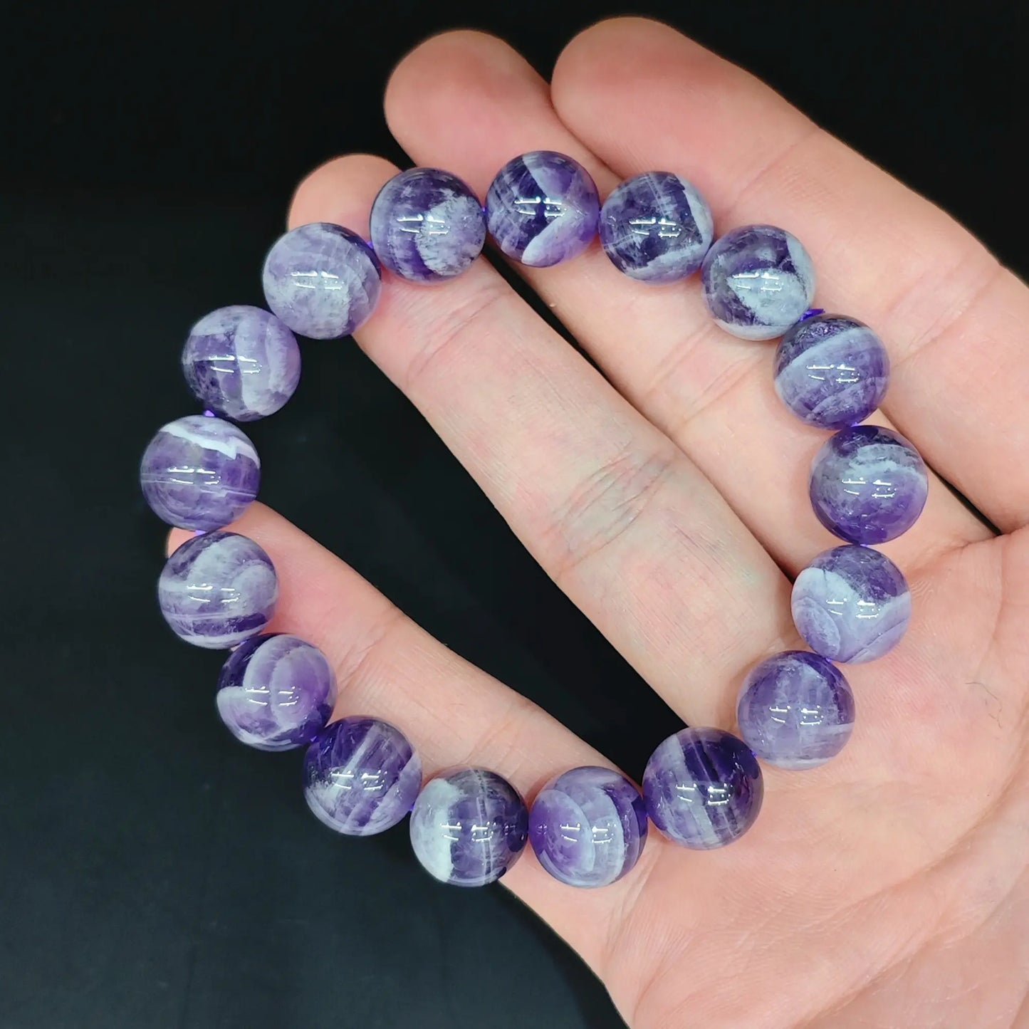 Natural dream chevron amethyst smooth round bead bracelet held close up showing rich purple tones and white quartz V bands