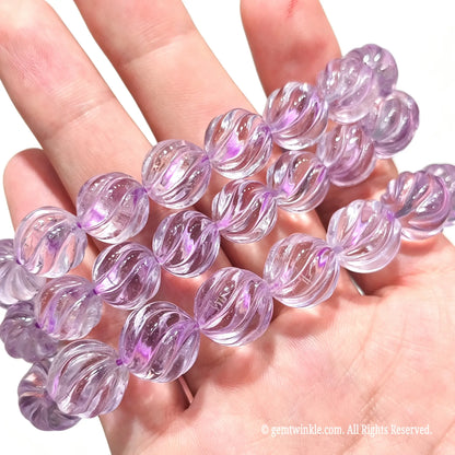 Stacked view of natural light purple amethyst spiral carved pumpkin bead bracelets in hand with high clarity