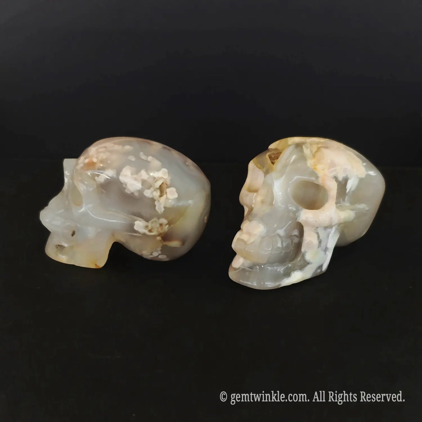 A hand holding a polished flower agate human skull carving to illustrate its 6cm length and flat stable base