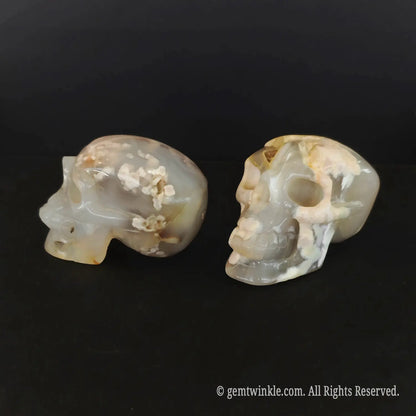 A hand holding a polished flower agate human skull carving to illustrate its 6cm length and flat stable base