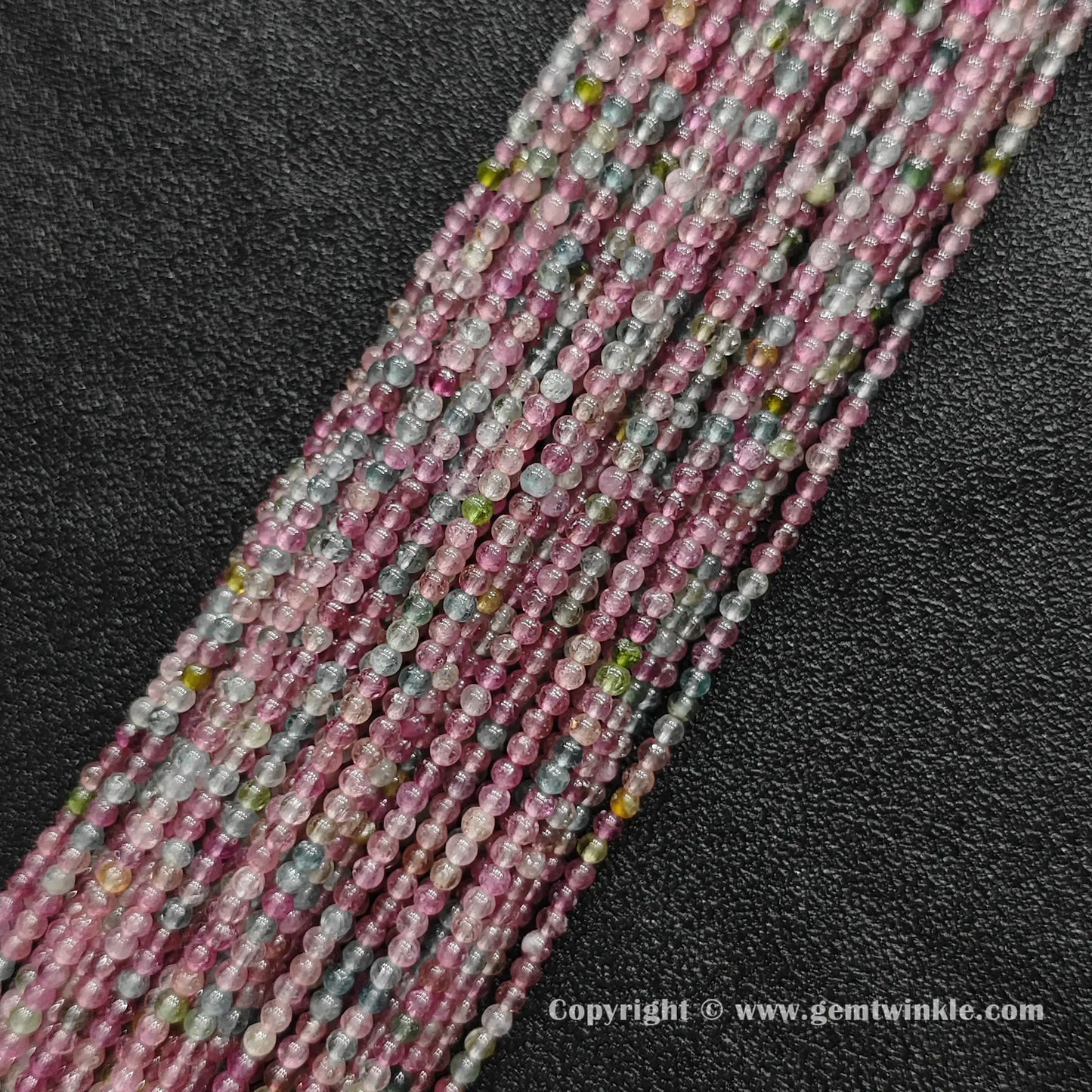 Multiple strands of pastel light color tourmaline 2.5mm micro round beads on dark background