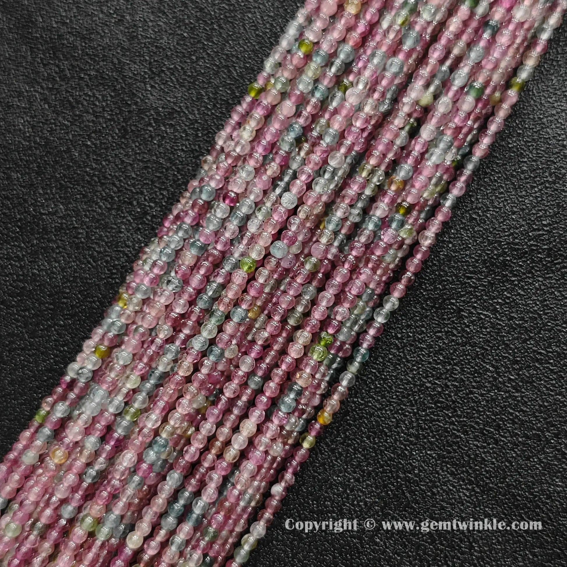 Multiple strands of pastel light color tourmaline 2.5mm micro round beads on dark background