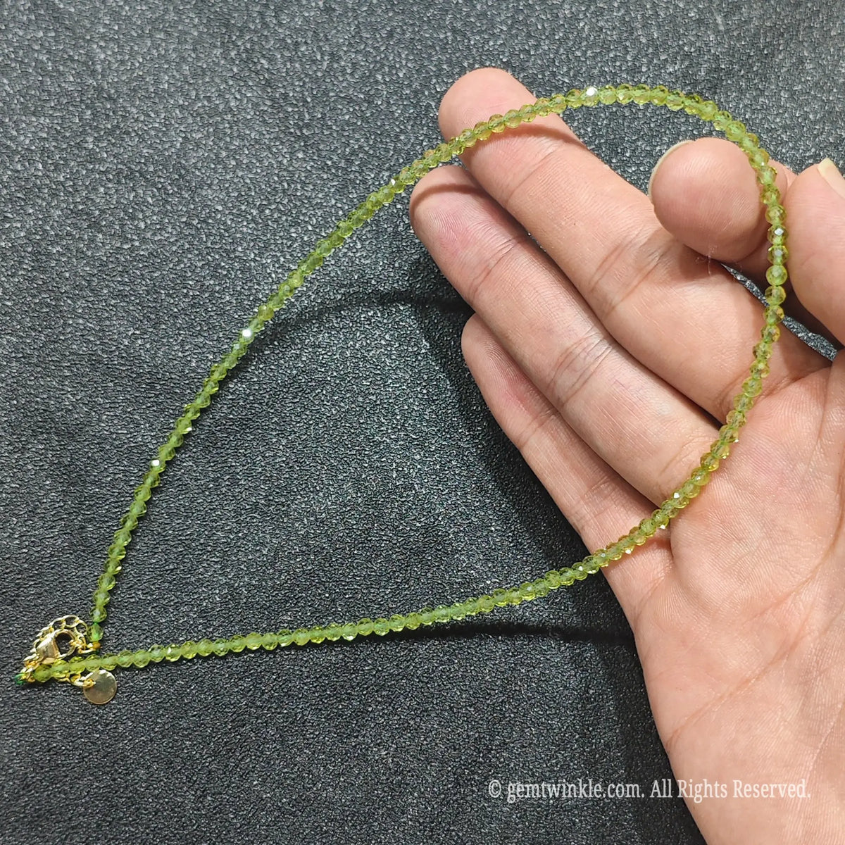 Hand holding 3mm micro faceted green peridot necklace strand revealing luminous olivine transparency