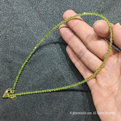 Hand holding 3mm micro faceted green peridot necklace strand revealing luminous olivine transparency
