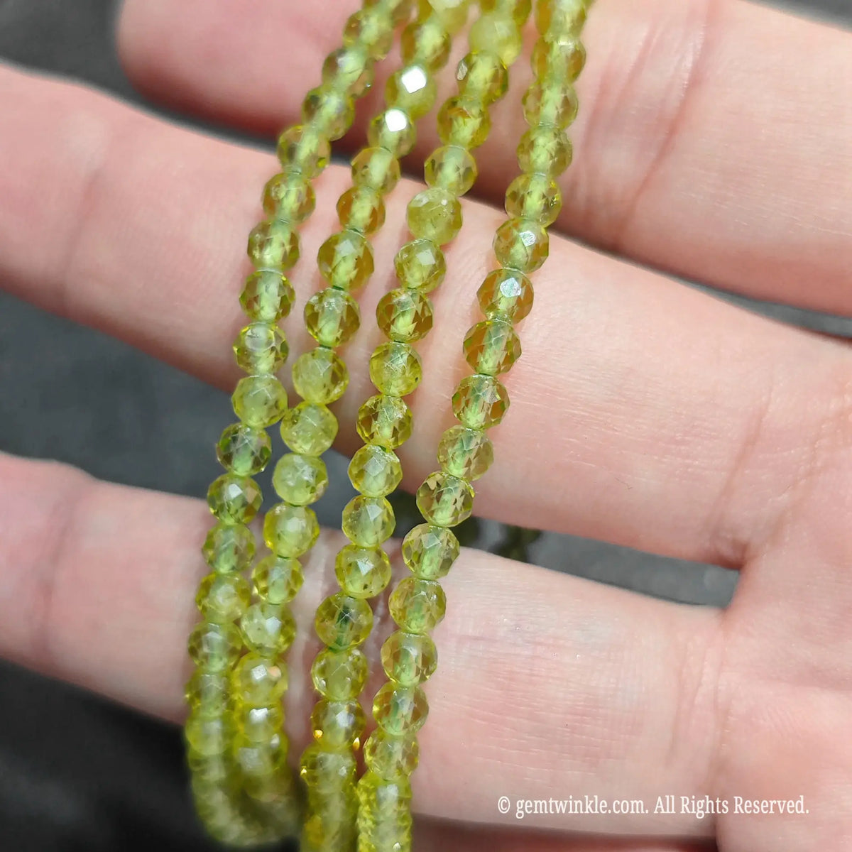 Side view of multiple natural peridot faceted round bead stretch bracelets held across fingers