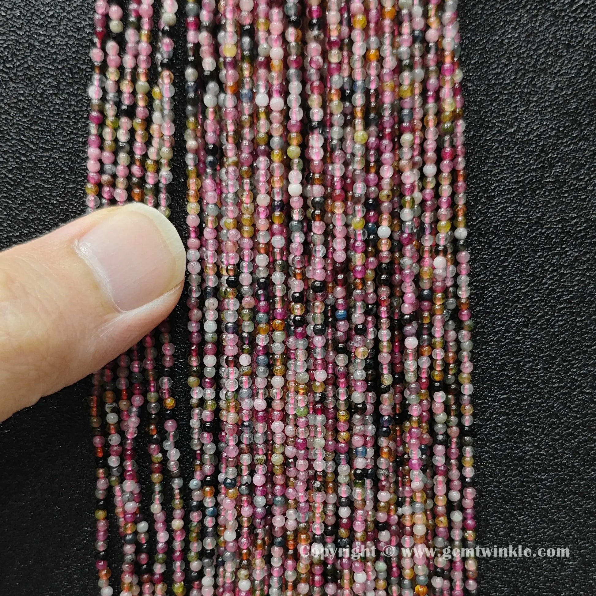 Angled view of petite semi translucent multi color tourmaline seed bead strands displaying polished luster