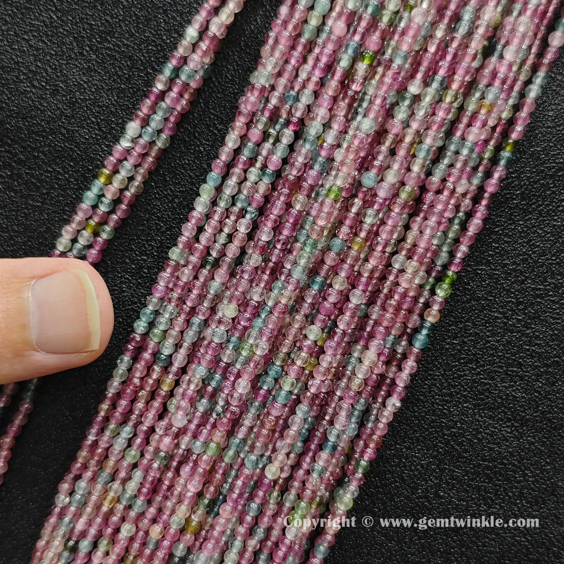 Finger holding petite light color tourmaline 2.5mm small bead strands demonstrating scale