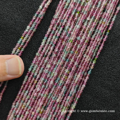Finger holding petite light color tourmaline 2.5mm small bead strands demonstrating scale