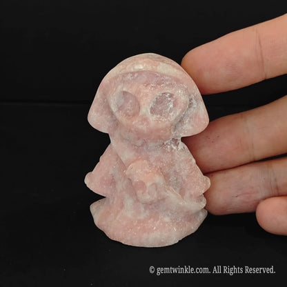 A 5cm natural pink opal cute grim reaper figurine being held by a human hand showing its smooth polished pastel pink textures