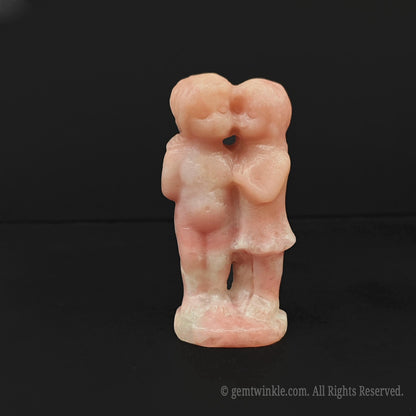 Front view of a 7cm natural pink opal kissing boy and girl statue highlighting smooth pastel pink tones