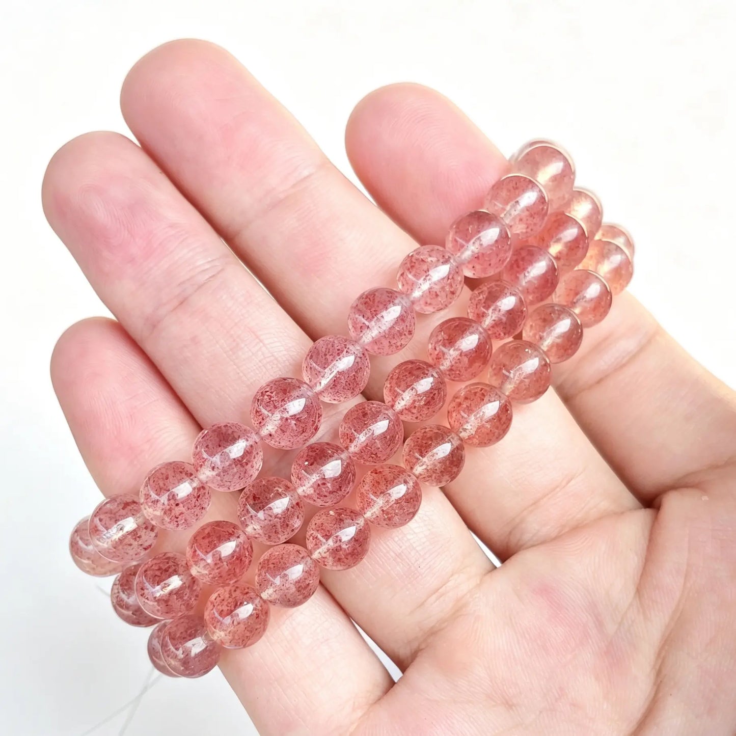 Main handheld view of pink strawberry quartzite round bead stretch bracelets stacked on open hand showing subtle red speckled inclusions