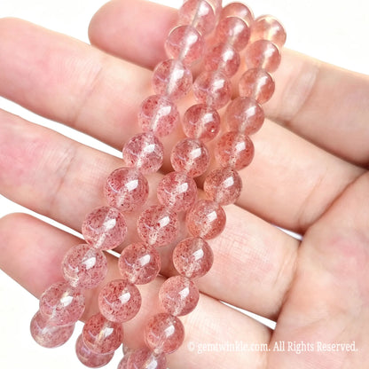 Pink strawberry quartzite round bead stretch bracelets arranged across open hand displaying soft translucent pink tones