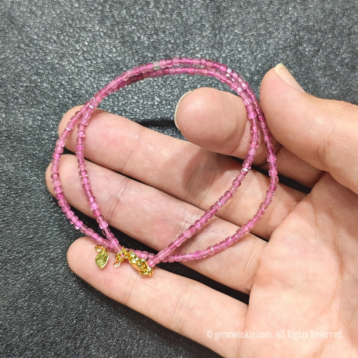 Hand holding 2.5mm precision cube cut Pink Tourmaline necklace strand showing vibrant magenta color clarity
