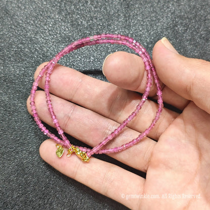 Hand holding 2.5mm precision cube cut Pink Tourmaline necklace strand showing vibrant magenta color clarity