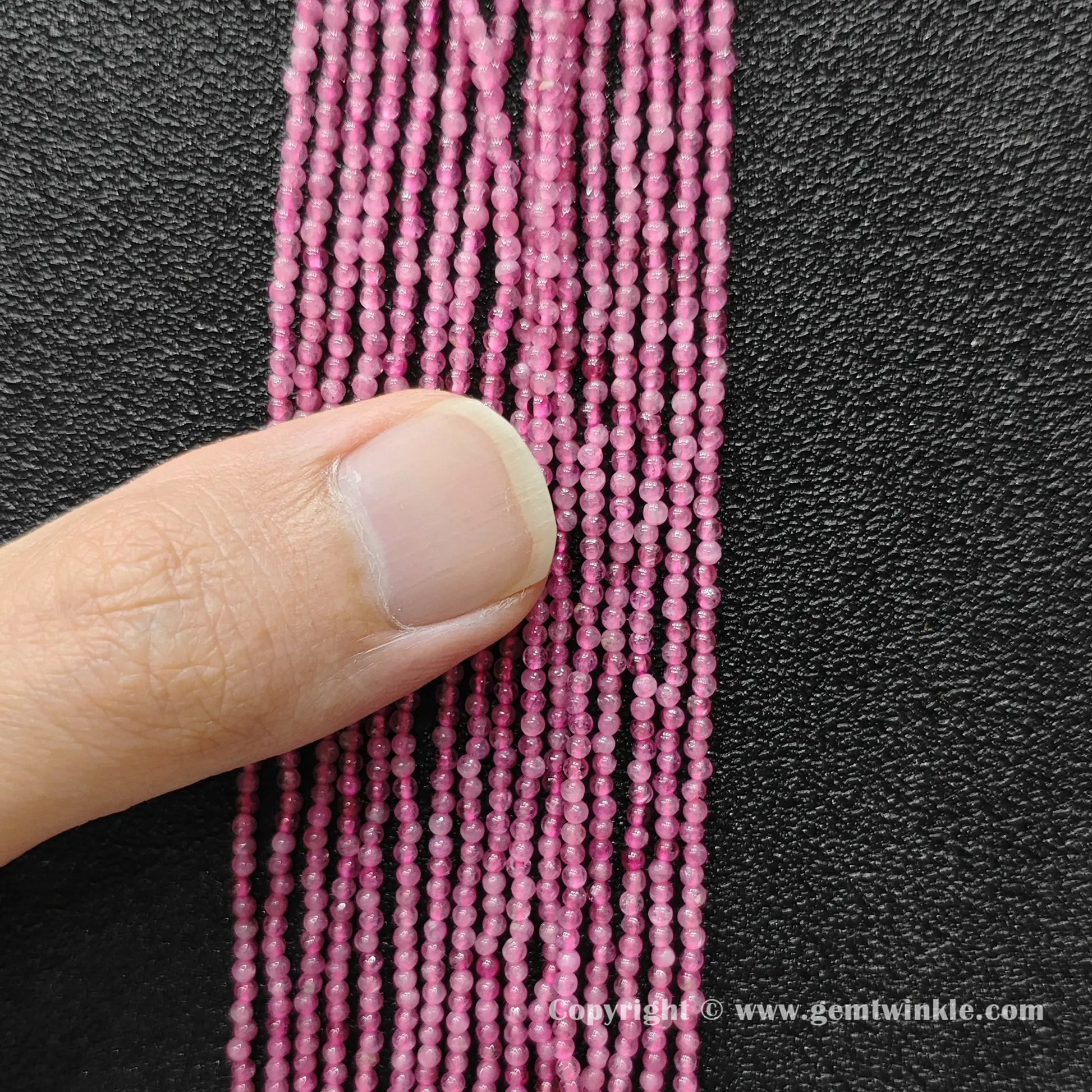 Finger holding natural pink tourmaline 2mm seed bead strands demonstrating scale for jewelry supply