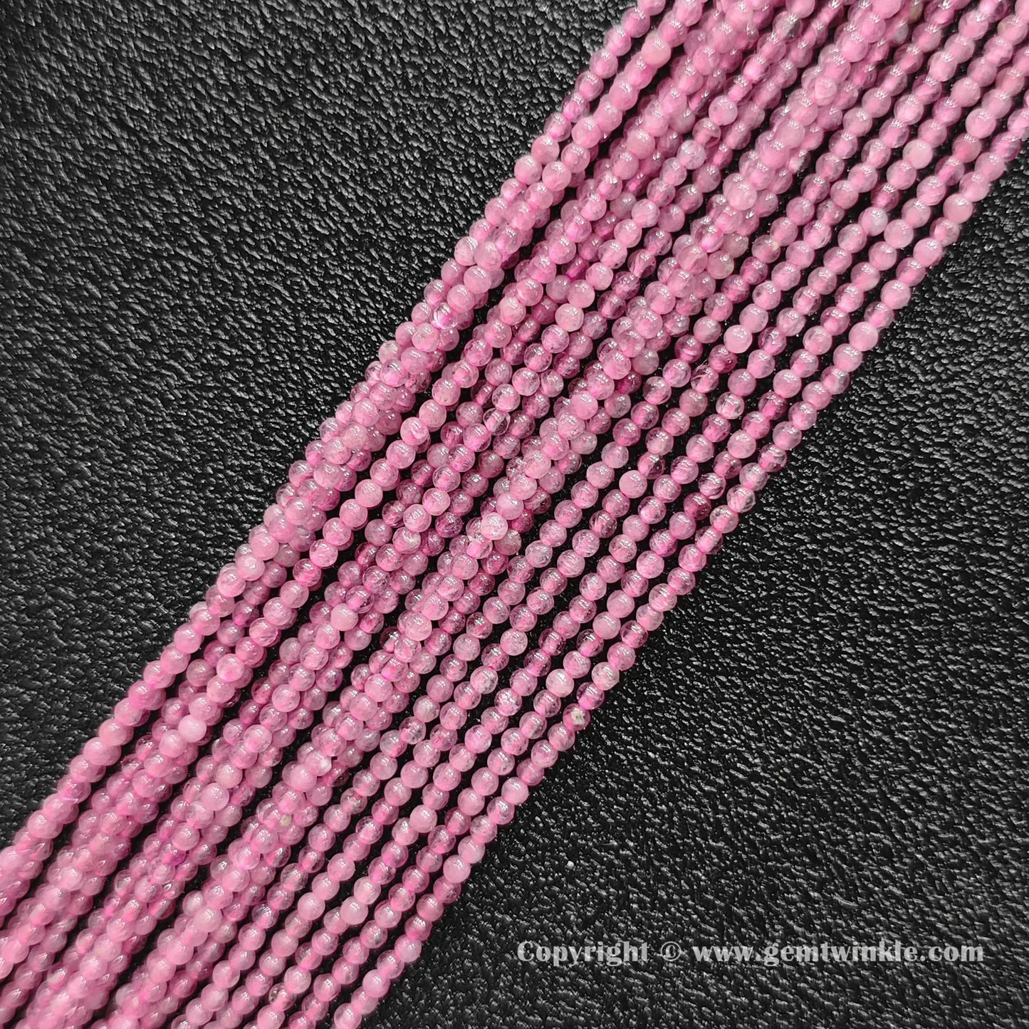 Multiple strands of natural pink tourmaline 2mm seed beads lined up on dark background