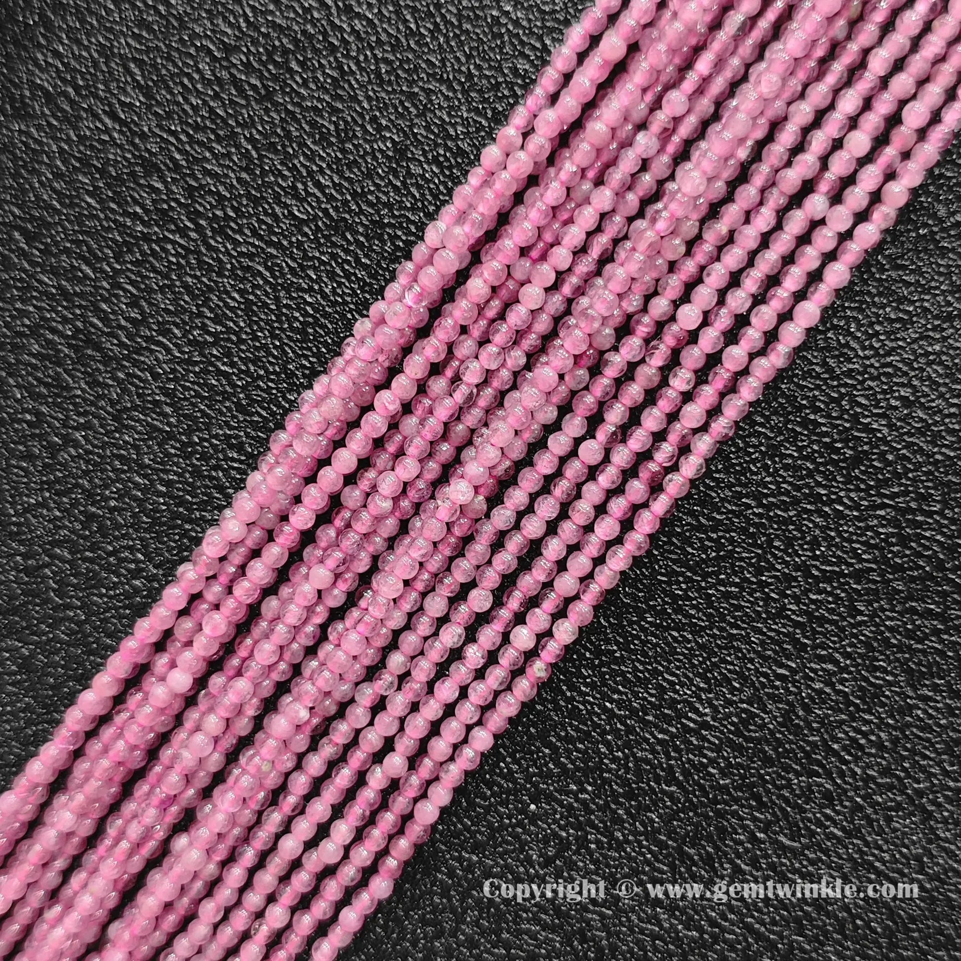 Multiple strands of natural pink tourmaline 2mm seed beads lined up on dark background