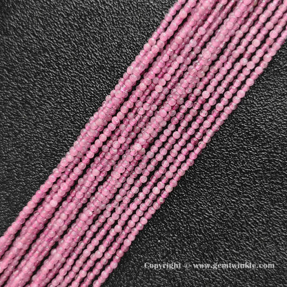 Multiple strands of natural pink tourmaline 2mm seed beads lined up on dark background