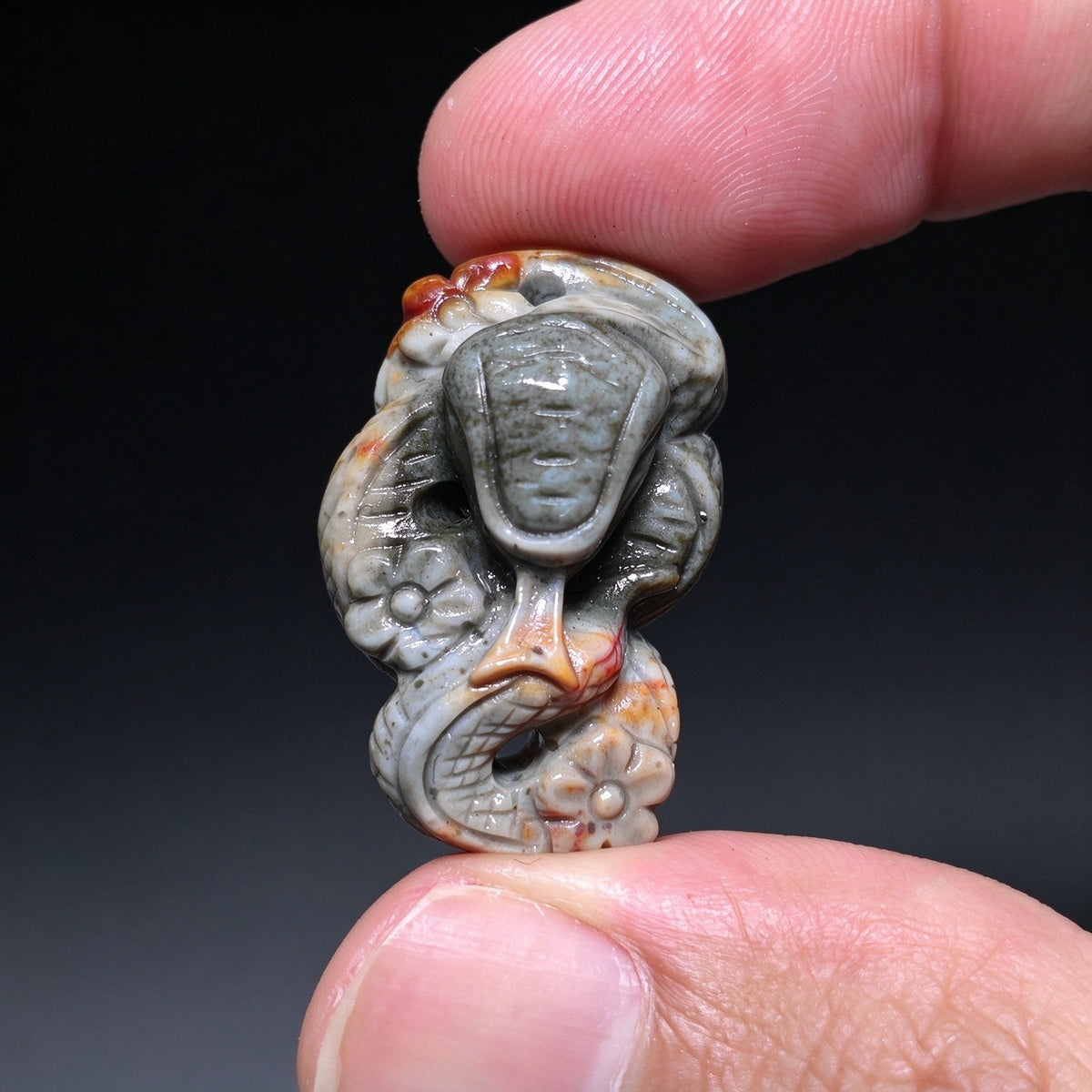 Top down view of a mini flat-laying carved stone snake with plum blossom details in slate gray and red held between fingers