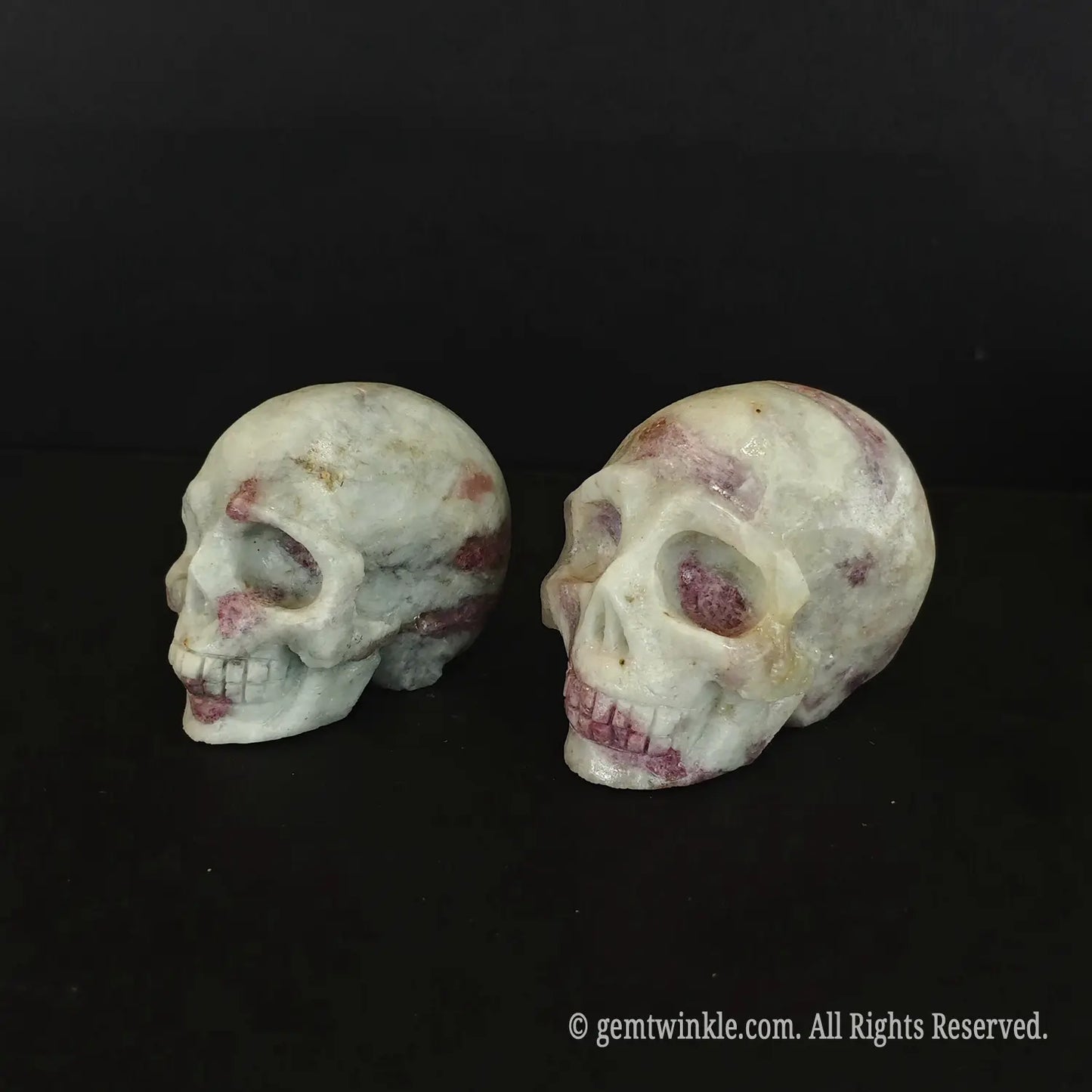Side profile of a 6cm pink tourmaline skull carving showing rosy mineral spots across the quartz crown
