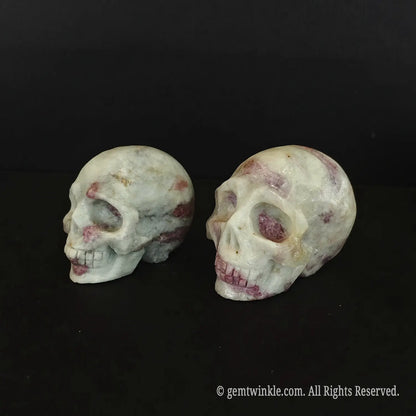 Side profile of a 6cm pink tourmaline skull carving showing rosy mineral spots across the quartz crown
