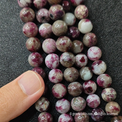 Plum blossom tourmaline round beads held in hand showing size scale and pink tourmaline matrix inclusions
