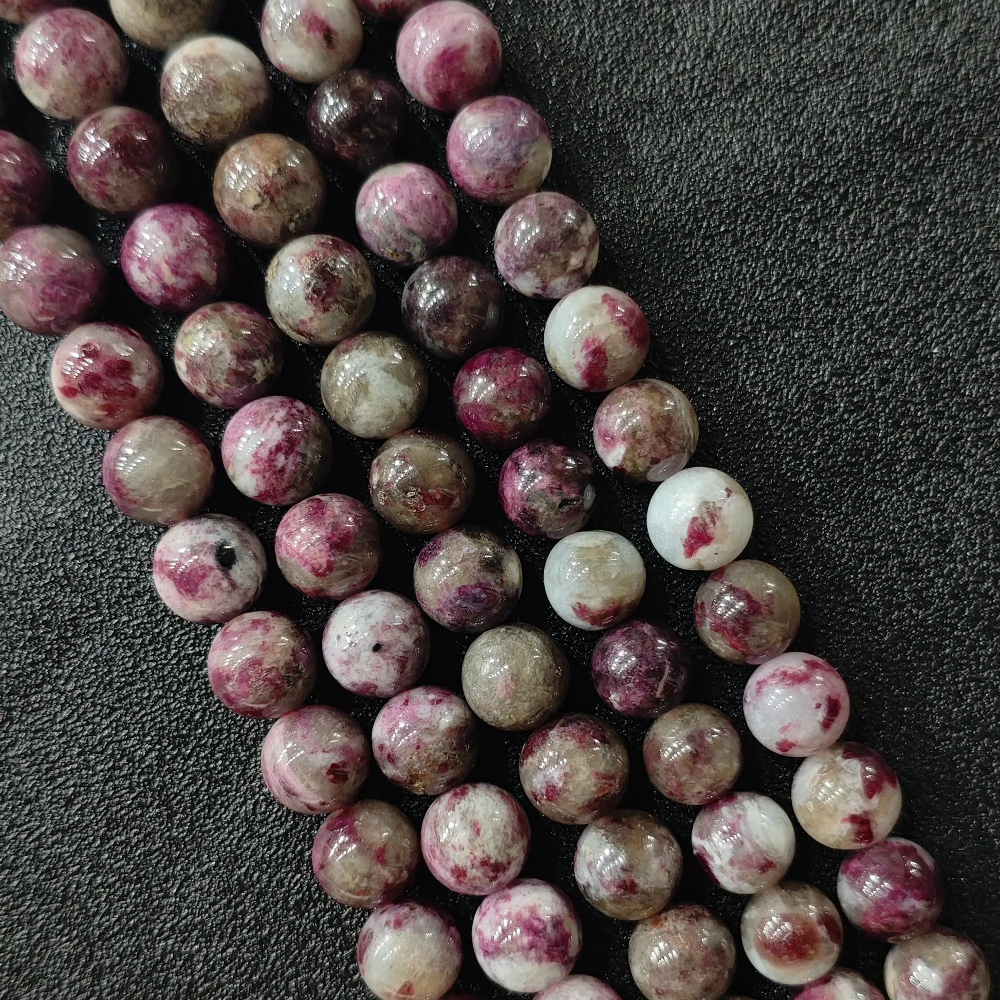 Plum blossom tourmaline round beads strand close up showing magenta pink speckled patterns on quartz base