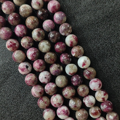 Plum blossom tourmaline round beads strand close up showing magenta pink speckled patterns on quartz base