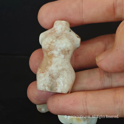 A close up of a hand holding a single 5cm pink flower agate goddess torso figurine showing detailed body contours and natural mineral inclusions