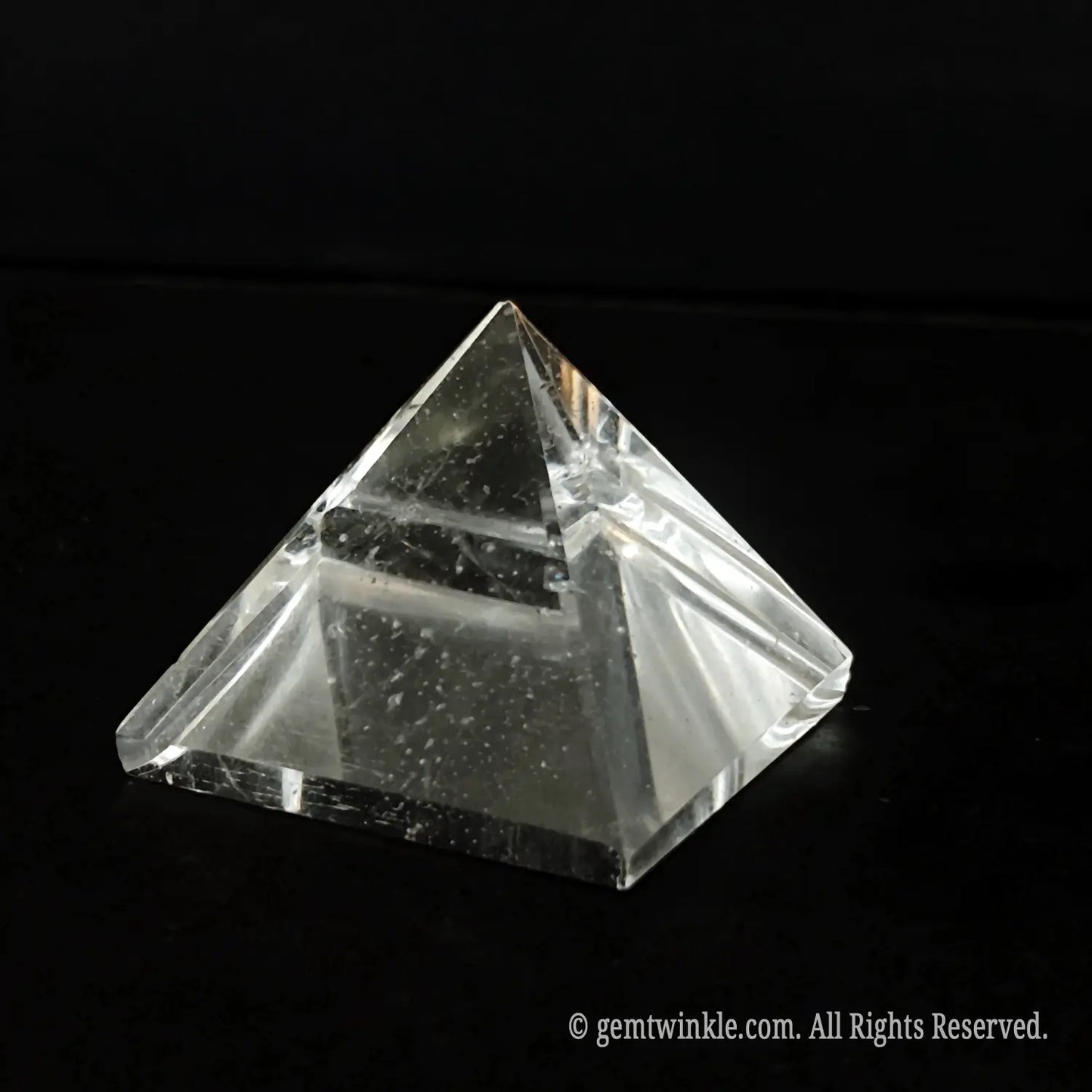 Side look of a polished four-sided clear quartz pyramid highlighting organic cloudy veils inside