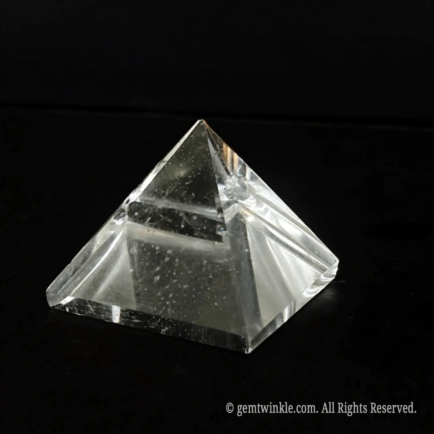 Side look of a polished four-sided clear quartz pyramid highlighting organic cloudy veils inside